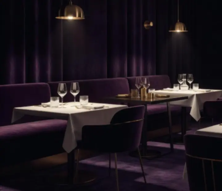 Salle de restaurant intimiste éclairée en lumière tamisée, tables dressées pour le dîner.